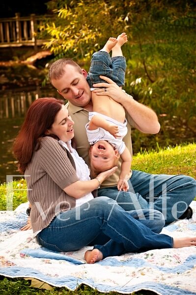 Mom and dad play with child outdoors on blanket